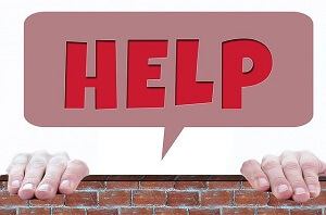 Two hands hanging on to the top of a wall with the words HELP coming from behind the wall