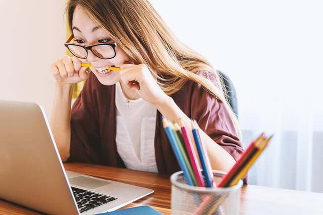 young woman studying hard at a laptop, biting on a pencil